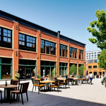 **Prompt:** A vibrant, mixed-use urban landscape showcasing a revitalized former factory. The building features exposed brick, large windows, and modern loft apartments. Street level includes trendy cafes with outdoor seating, artisan shops, and pedestrian walkways bustling with people. Incorporate lush green spaces with trees and public art installations. The overall atmosphere is energetic, sustainable, and community-focused, illustrating successful urban regeneration by URC. Style: Photorealistic, warm lighting.